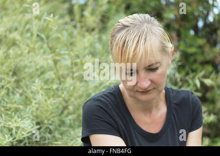 Porträt der frustrierte Frau alles Alters.  Blonde Womani im schwarzen Hemd ist draußen sitzen. Sie hat gesenktem Kopf. Stockfoto