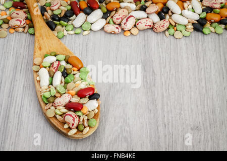 Gemischte getrocknete Hülsenfrüchte und Getreide in Holzlöffel auf grauem Hintergrund aus Holz. Textfreiraum Stockfoto
