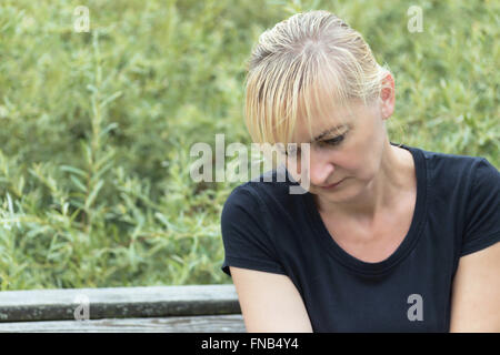 Porträt der frustrierte Frau alles Alters.  Blonde Womani im schwarzen Hemd sitzt auf einer Bank vor. Stockfoto