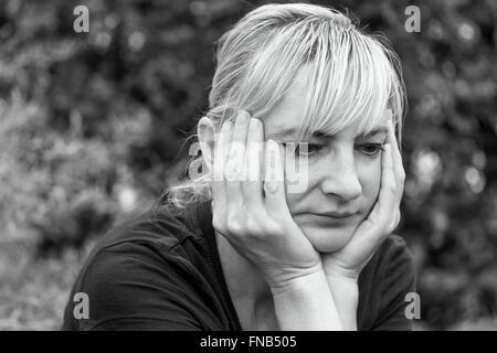 Side  portrait of a frustrated middle aged woman, who is supporting her face by hands and is looking ahead. Stockfoto
