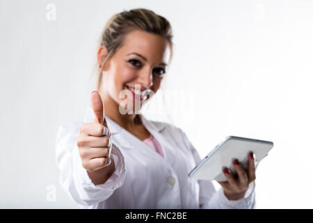 lächelnde Frau ist ein Arzt hält eine Tablette und zeigt einen Daumen IN FOCUS auf Vordergrund unscharf und es gibt eine weiße backg Stockfoto