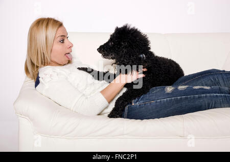 Frau liegend auf einem weißen Sofa mit einem schwarzen Pudel. Stockfoto