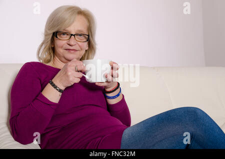 Ältere Frau auf einem weißen Sofa sitzen und Tee trinken. Stockfoto