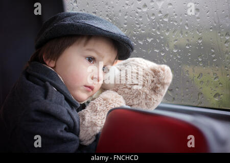 Süßes kleines Kind, Vorschule junge, Reiten in einem Bus, tagsüber, hält Teddybär Stockfoto