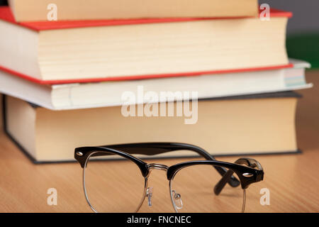 Paar schwarze Felge Brille neben einen Stapel Bücher auf einem Tisch Wodden Verlegung Stockfoto