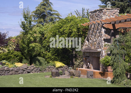 Einen massiven Kamin mit Steinen sitzen vor ihm in einem schön angelegten Garten mit einem trockenen Steinmauer im backgroun Stockfoto