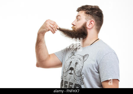 Profil von schockiert gefragt bärtiger Mann hält seinen Bart über weißem Hintergrund Stockfoto