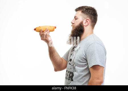 Profil von attraktiven bärtiger Mann stehen und halten Hotdog auf weißem Hintergrund Stockfoto