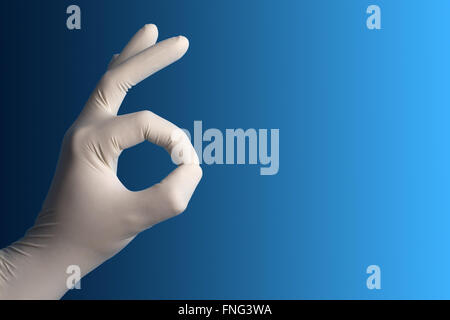 Hand mit einem weißen Operationshandschuh zeigt die ok Zeichen auf blauem Grund Stockfoto