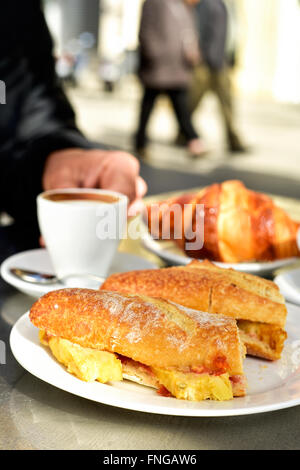 Mann sitzt in einem Tisch auf der Terrasse eines Cafés setzen zum Frühstück, mit einigen Tassen Kaffee, ein Croissant und ein spanisches Omelett Stockfoto