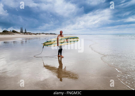 Ein junger Mann geht Surfen, waipu Cove, Waipu, Northland, Neuseeland Stockfoto