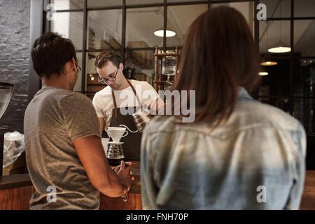 Paar an einem Café-Schalter mit Barista Kaffee gießen Stockfoto