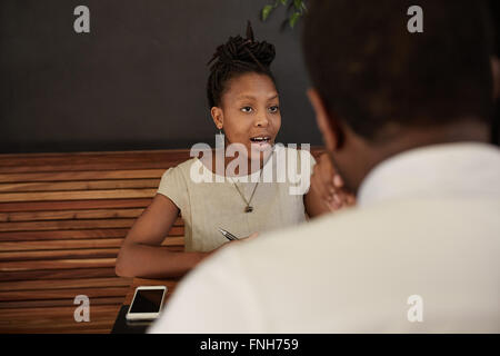 Afrikanische Frau, die selbstbewusst in einem modernen Café im Gespräch Stockfoto