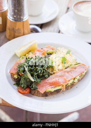 Abgestürzte Avocado und Lachs Vollkorn Toast serviert mit Rührei, sautierten Spinat und Kirschtomaten. Stockfoto