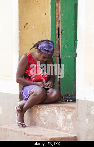 Alltag in Kuba - kubanische Frau sitzt vor Haustür mit Perlen in Trinidad, Kuba im März Stockfoto