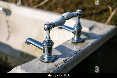 Alt, verlassene Keramik Bad und Chrom Wasserhähne wie in einem Feld gesehen, mit dem Bad als Wassertrog verwendet. Stockfoto