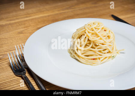 Spaghetti mit Knoblauch, Öl und Peperoni mit Petersilie und Gabel am Tisch Stockfoto