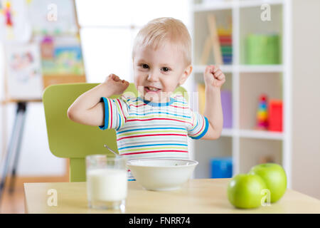 Kind junge, gesunde Ernährung und zeigt seine Stärke im Innenbereich Stockfoto