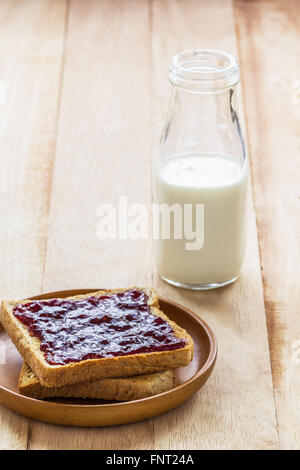 Toast mit Marmelade in hölzernen Platte und Milch Flasche auf Holztisch Stockfoto