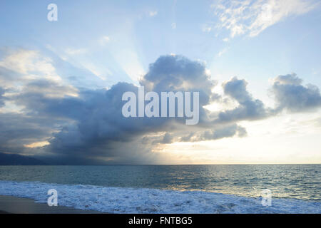 Sun Ray Wolken leuchtet hell Licht golden Seelandschaft mit Wellen ans Ufer Rollen, als vereinzelte Sonnenstrahl durch bricht. Stockfoto