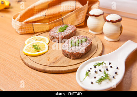 Rohe Schnitzel mit Zitronenscheiben auf ein Schneidebrett Stockfoto