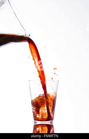 Trinken Sie, kräftig gegossen aus einer Karaffe, überfüllt, spritzt aus einem Glas auf weißem Hintergrund Stockfoto