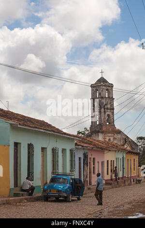 Alltag in Kuba - arbeiten am Auto in der Straße mit zerstörten Kirche Iglesia de Santa Ana in der Ferne auf Trinidad, Kuba im März Stockfoto