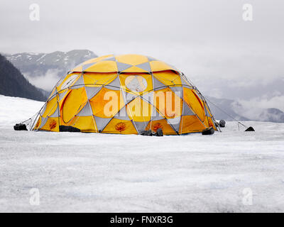 Camping im Hochgebirge. Orange und grau Zelt auf dem Gletscher. Stockfoto