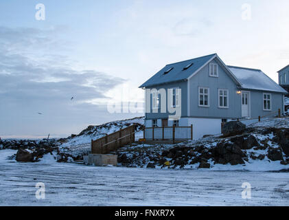 Holzhaus thront auf schneebedeckten Felsen, bei Sonnenaufgang in Stykkisholmur, Island Stockfoto