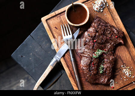 Beefsteak. Stück Rindfleisch vom Grill BBQ mariniert mit Gewürzen und Kräutern auf rustikalem Holzbrett über groben hölzernen Schreibtisch mit Textfreiraum Stockfoto