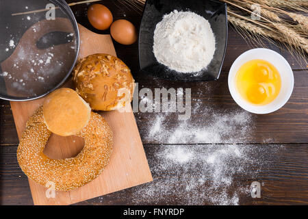 Verschiedene Brötchen mit Backzutaten einschließlich Eiern und Mehl in Schalen Aufwand auf einen Holztisch mit Ähren angesehen. Stockfoto