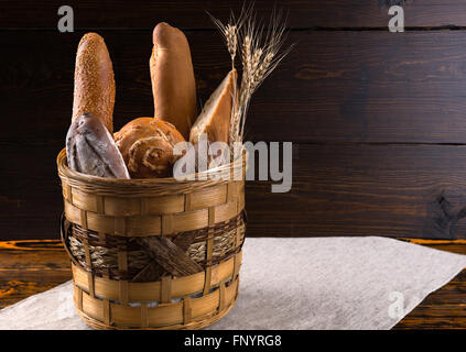 Verschiedene Brote an Brot, Brötchen und Baguettes in einem rustikalen Korb auf einem alten Holztisch mit einem hölzernen Hintergrund mit Textfreiraum Stockfoto