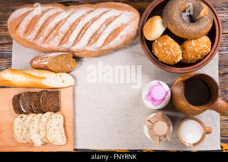 Top-down Ansicht von Brot Brote, Scheiben, Brötchen, Bagels und Milchflaschen auf Tuch über Holztisch Stockfoto