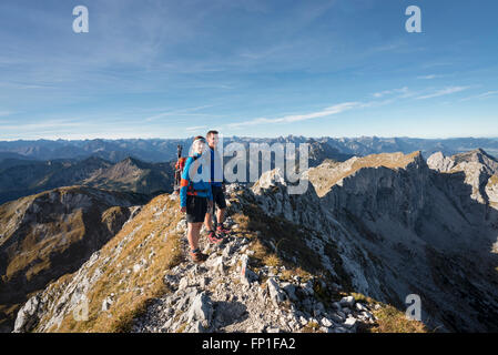 Wanderern stehen auf dem Gipfelgrat des Mount Hochplatte mit dem Panorama der Ammergauer Alpen an einem Herbstmorgen, Bayern, Deutschland Stockfoto