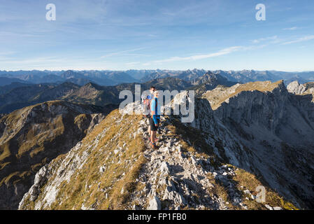 Wanderern stehen auf dem Gipfelgrat des Mount Hochplatte mit dem Panorama der Ammergauer Alpen an einem Herbstmorgen, Bayern, Deutschland Stockfoto