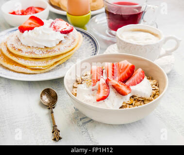 Frühstück Essen mit Müsli, Joghurt und Erdbeeren, Tee, Kaffeetasse und Pfannkuchen Stockfoto