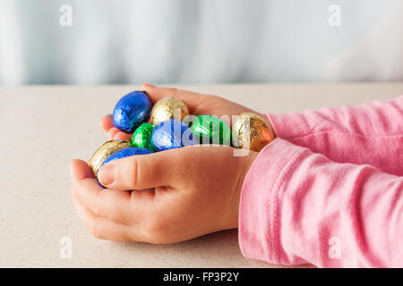 Des Kindes Hände halten Schokoladeneier in bunte Folie mit textfreiraum gewickelt. Seitenansicht. Stockfoto