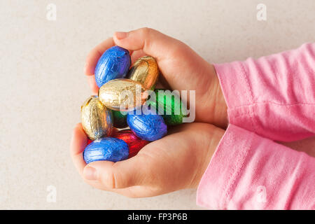 Des Kindes Hände halten Schokoladeneier in bunte Folie mit textfreiraum gewickelt. Ansicht von oben. Stockfoto