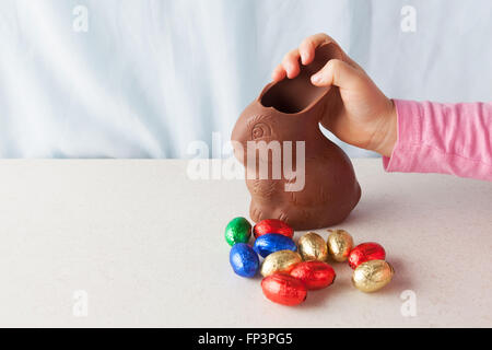 Kind an der Hand ein Ohr aus Schokolade Osterhasen mit textfreiraum zu brechen. Stockfoto