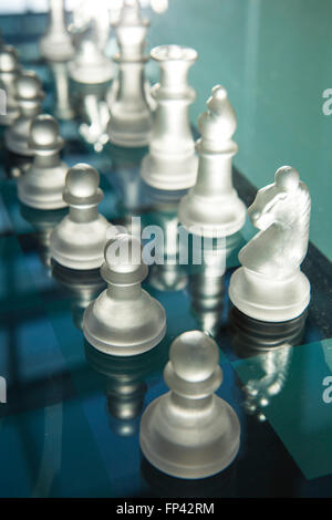 Stücke von einem Glas oder einer harten Kunststoff Schach set Leuchten sind Hintergrundbeleuchtung durch die tiefstehende Sonne durch ein Fenster. Stockfoto