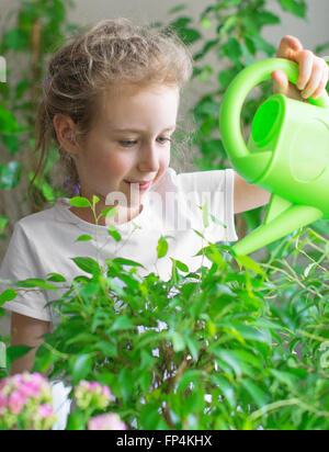 Niedliche kleine Mädchen Bewässerung Blumen zu Hause. Stockfoto