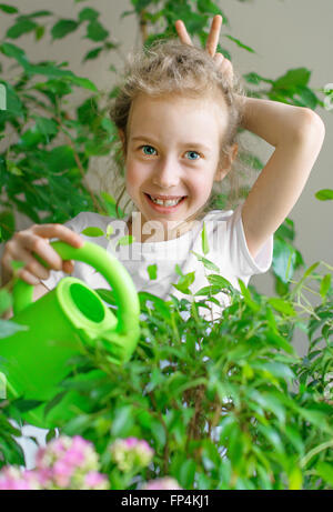 Niedliche kleine Mädchen Bewässerung Blumen zu Hause. Stockfoto