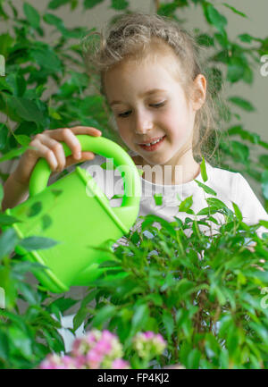 Niedliche kleine Mädchen Bewässerung Blumen zu Hause. Stockfoto