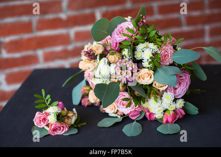 Wunderschönen Brautstrauß von frischen Blumen und Bräutigam Boutonniere auf alten schwarzen Holztisch in rotem Backstein-Mauer-Hintergrund Stockfoto