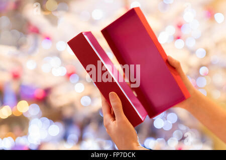 Frau öffnet ein rotes Geschenk vor einem Weihnachtsbaum Stockfoto