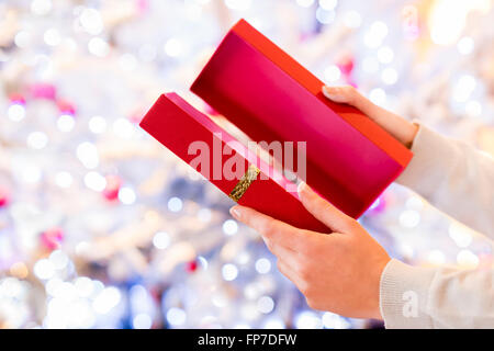 Frau öffnet ein rotes Geschenk vor einem Weihnachtsbaum Stockfoto