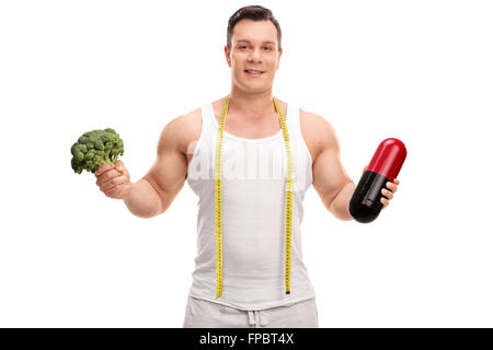 Junger Mann mit einem Stück von Broccoli in der einen Hand und einem großen Diät-Pille in den anderen isoliert auf weißem Hintergrund Stockfoto