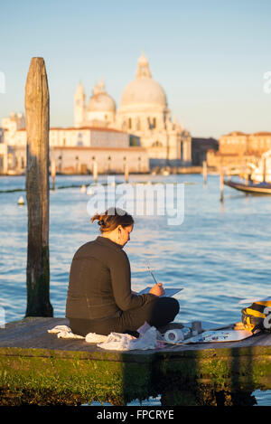 Frau sitzt auf einem Steg in der Nähe des Markusplatzes bei Sonnenaufgang malen das Stadtbild von Venedig am Canal Grande Stockfoto