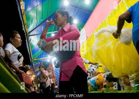 Eine Frau arbeitet auf ein Arcade-Spiel, wo Menschen werfen Darts auf Ballons an einem Strassenfest in Kampong Cham, Kambodscha. Stockfoto