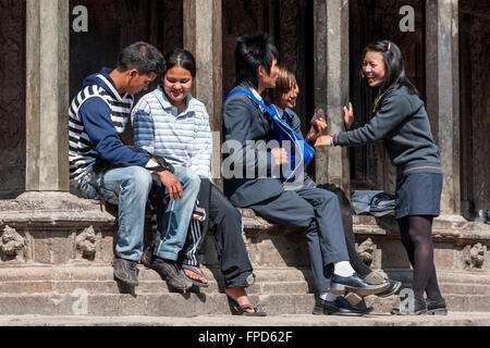 Nepal, Patan.  Junge Männer und Frauen reden in Durbar Square, sitzen am Rand eines Tempels. Stockfoto